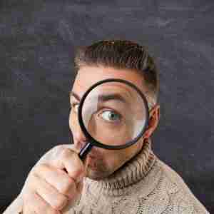 Man holding magnifying glass over eye.