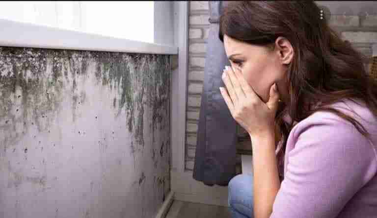 Woman covering nose, moldy wall background.